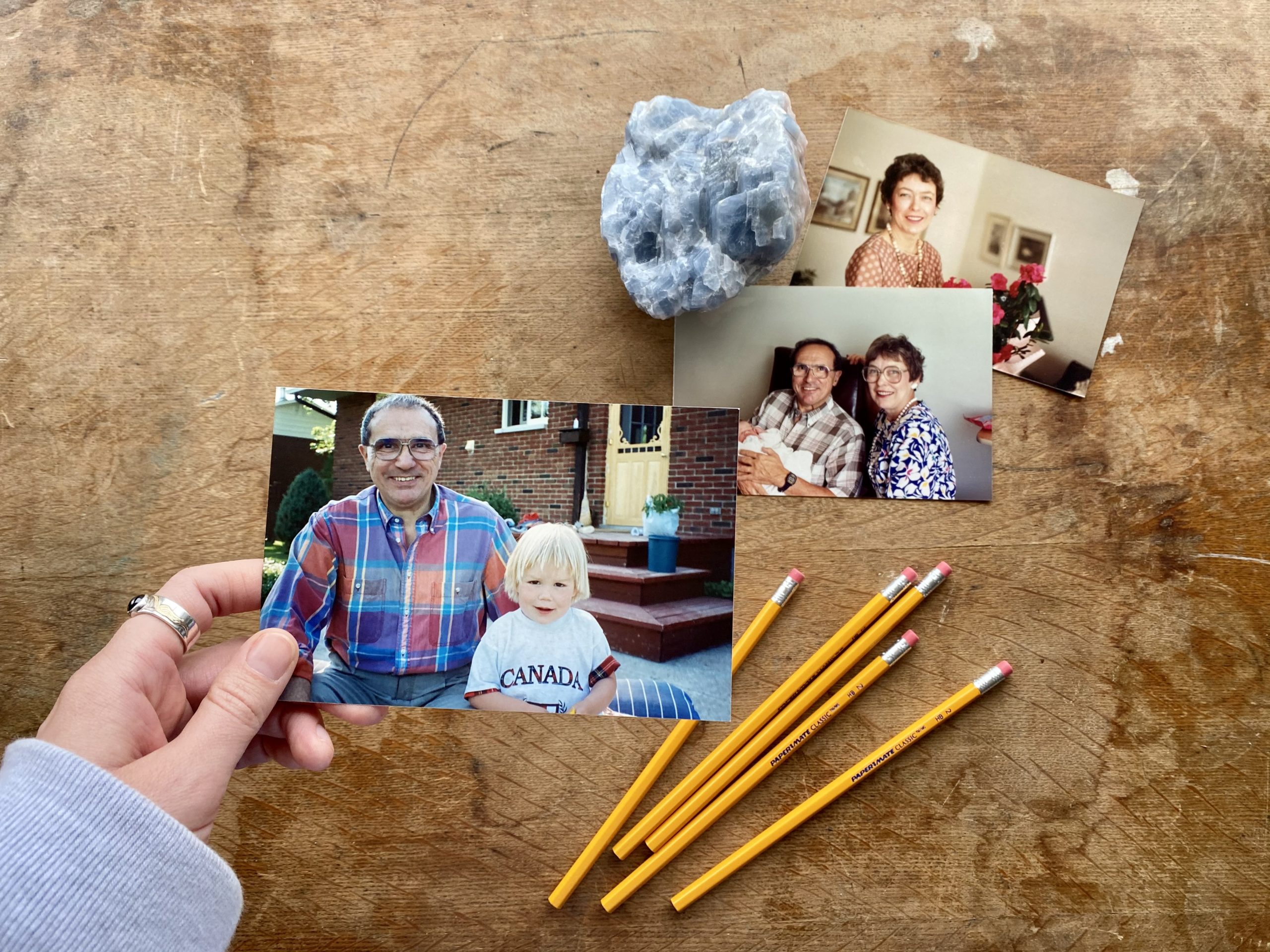 A woman holds a picture of a young blonde girl and her grandpa above a desk with two other pictures of her grandparents, a crystal and pencils